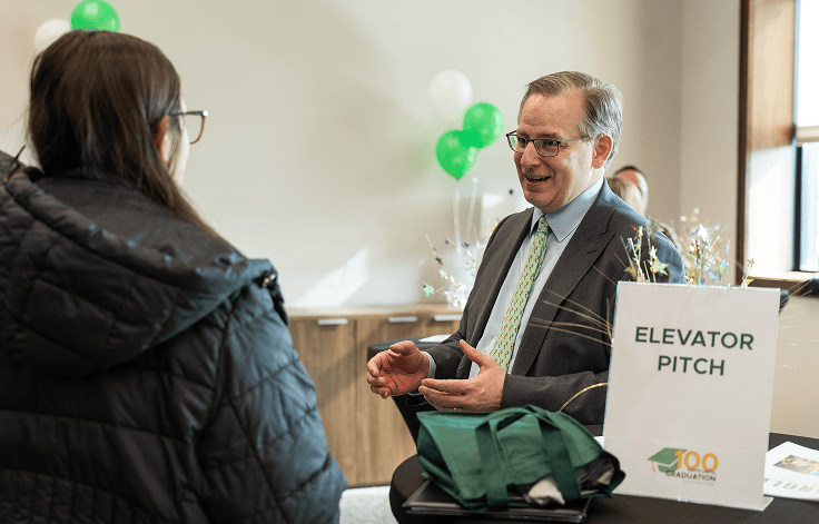 man near elevator pitch stand with student listening in front of him