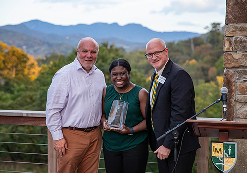 Alumna receiving an award during an outdoor ceremony with campus mountains in the background