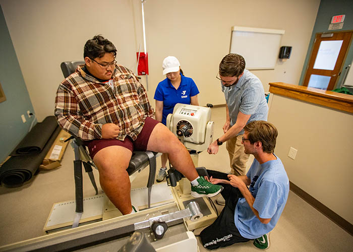 Students assist a participant measuring leg strength during a supervised exercise science lab session.