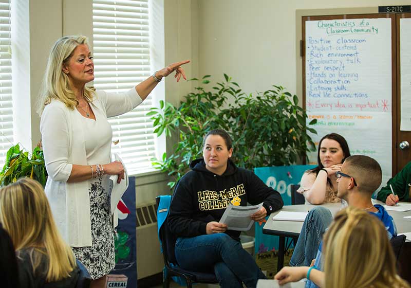 Instructor leads a classroom discussion as students listen and take notes.