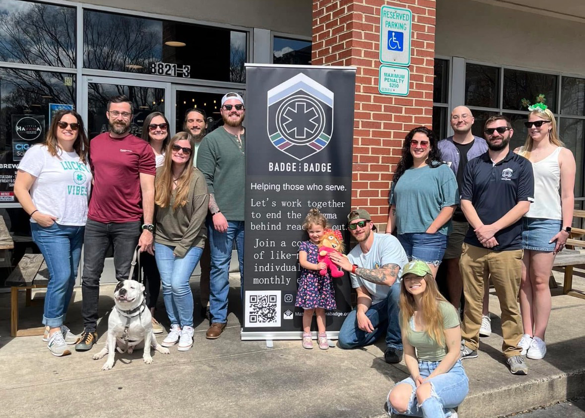 A group of people stand outside a business with a large Badge for Badge banner.