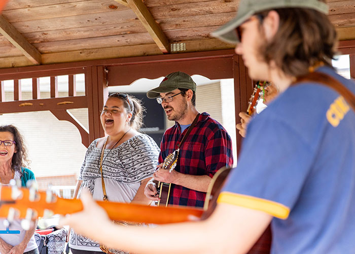 Faculty playing string instruments and singing together under a covered outdoor space