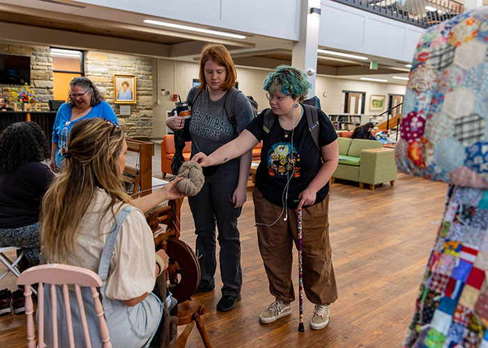 Students observing and participating in a fiber spinning demonstration indoors