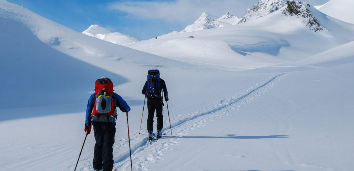 Two skiers hiking up a wide snow area with mountains in the background
