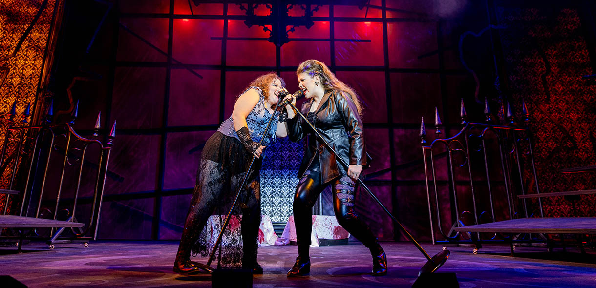 Two female performers singing on stage in rock music apparel in the show "Lizzie."